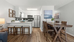 A modern kitchen with white cabinets, stainless steel appliances, and a wooden dining table with chairs. - Laguna Beach Community | Steps to Beach • Shared Pool + Pickleball | Gulf Walk (Panama City Beach)