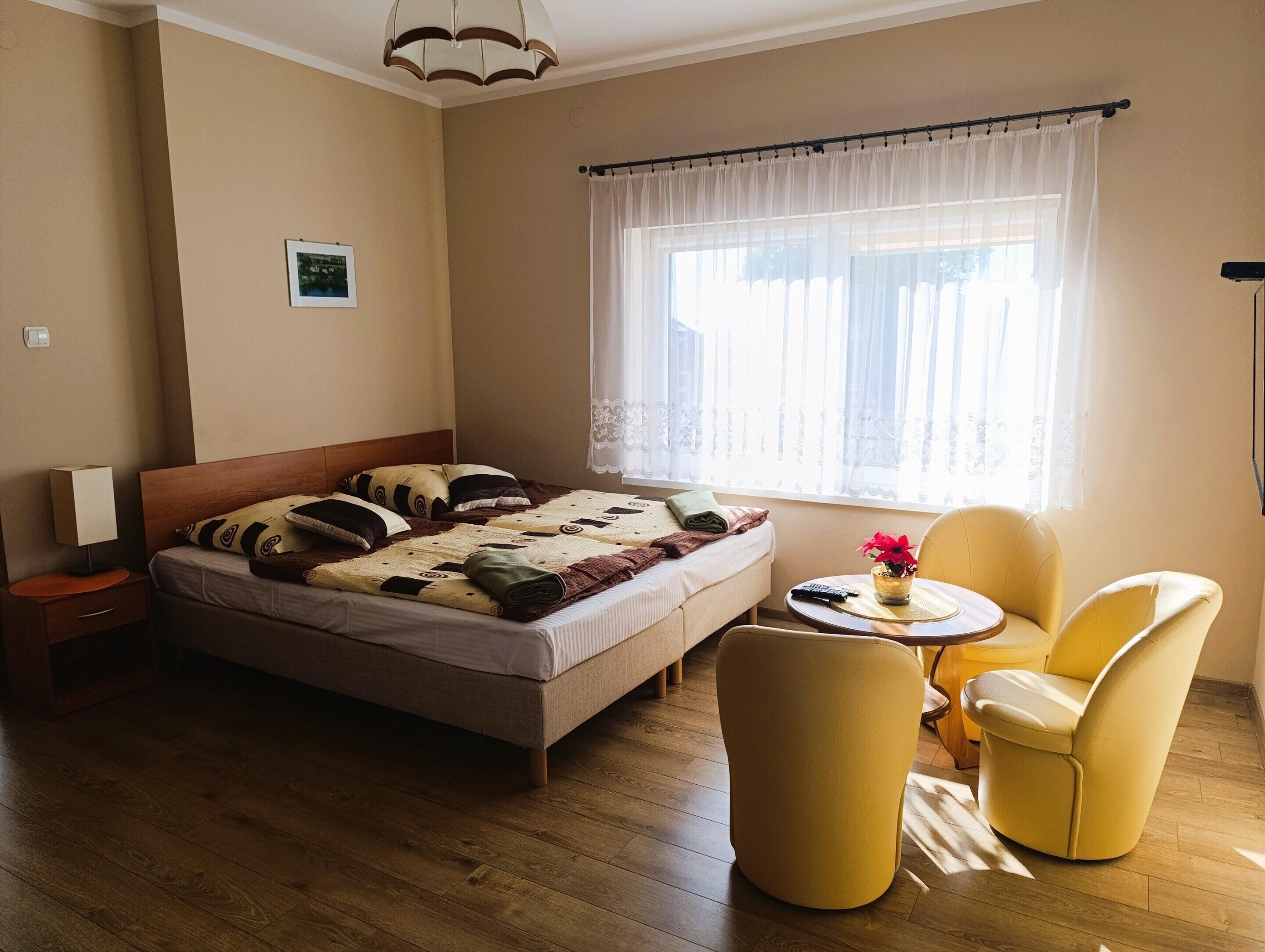 Een slaapkamer met een bed, nachtkastje, lamp, raam met gordijnen en twee stoelen.