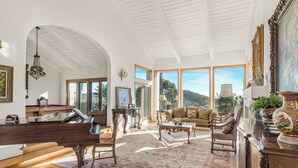 Amplia sala de estar con un piano de cola, asientos cómodos, ventanas grandes y vistas al exterior.