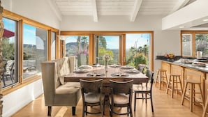 Un comedor con una mesa de madera dispuesta para seis personas, rodeada de sillas, y vistas al exterior a través de amplios ventanales.