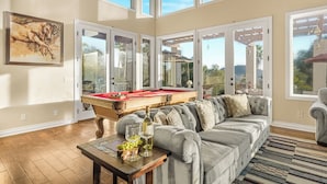 Amplia sala de estar con mesa de billar, asientos cómodos y grandes ventanales con vistas al exterior.