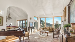 A spacious living room with a grand piano, comfortable seating, large windows, and a view of the outdoors. - Resort-Style Estate • Pool + Game Room + Tennis Court | The Tennis Ranch (Escondido)