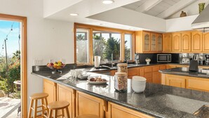 A modern kitchen with wooden cabinets, a granite countertop, and a large window overlooking a garden. - Resort-Style Estate • Pool + Game Room + Tennis Court | The Tennis Ranch (Escondido)