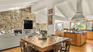 A spacious living area with a stone fireplace, a wooden dining table, and a kitchen island. - Resort-Style Estate • Pool + Game Room + Tennis Court | The Tennis Ranch (Escondido)