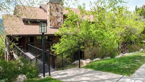 Un bâtiment à deux étages, doté d’une cheminée en pierre, d’un porche couvert et d’un escalier métallique menant à l’entrée.