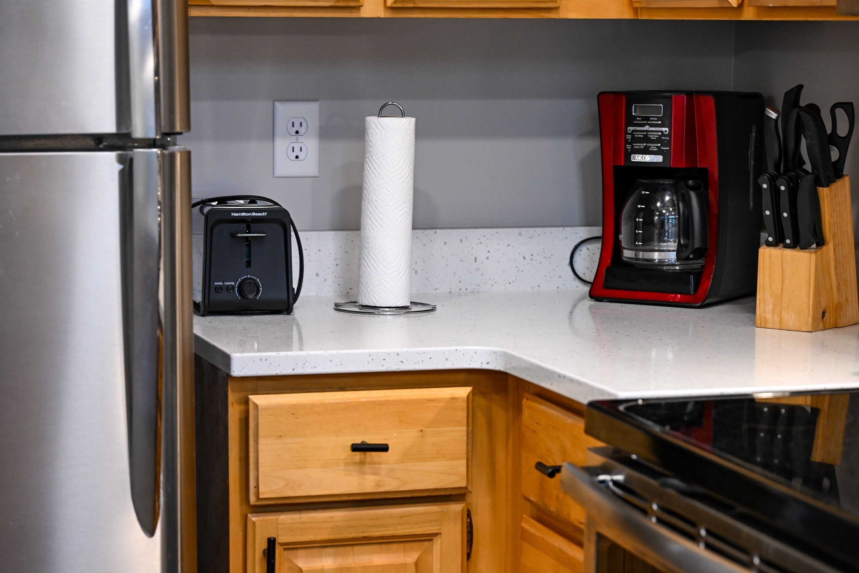 Une cuisine équipée d’un réfrigérateur en acier inoxydable, d’un grille-pain de la marque Hamilton Beach, d’un porte-essuie-tout, d’une machine à café rouge et d’un bloc à couteaux.