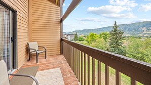 Un balcon doté de balustrades en bois, d’une chaise et offrant une vue sur un paysage verdoyant, avec des arbres et des collines.