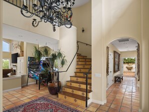 A spacious interior with a staircase, a chandelier, and a large potted plant.