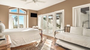 Habitación de hotel con dos camas, ventilador de techo, ventana grande con vistas y puerta corrediza que da a un área exterior.
