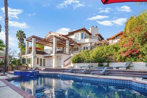Uma casa de dois andares com piscina, móveis de jardim e um jardim.