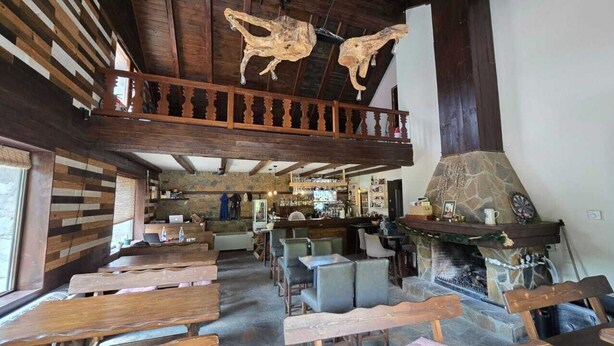 A rustic interior with wooden beams, a stone fireplace, and a bar area. - katafigio seli (Veroia)