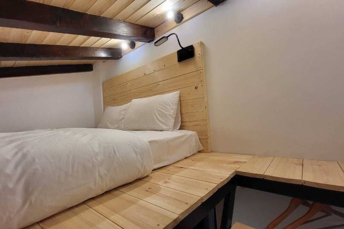 Quarto pequeno e acolhedor com uma cama beliche de madeira, uma escrivaninha de madeira e uma luminária na parede.