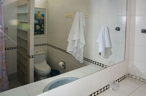 A bathroom with a toilet, a sink, and a shower. There are towels hanging on hooks and a poster on the wall. - w* | Modern 5BR with Private Pool in Paracas (Paracas)
