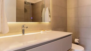 Un baño moderno con un lavamanos amplio, espejo y retrete.