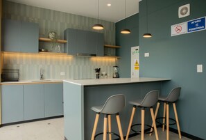 A modern kitchen with grey cabinets, a white countertop, and three bar stools.