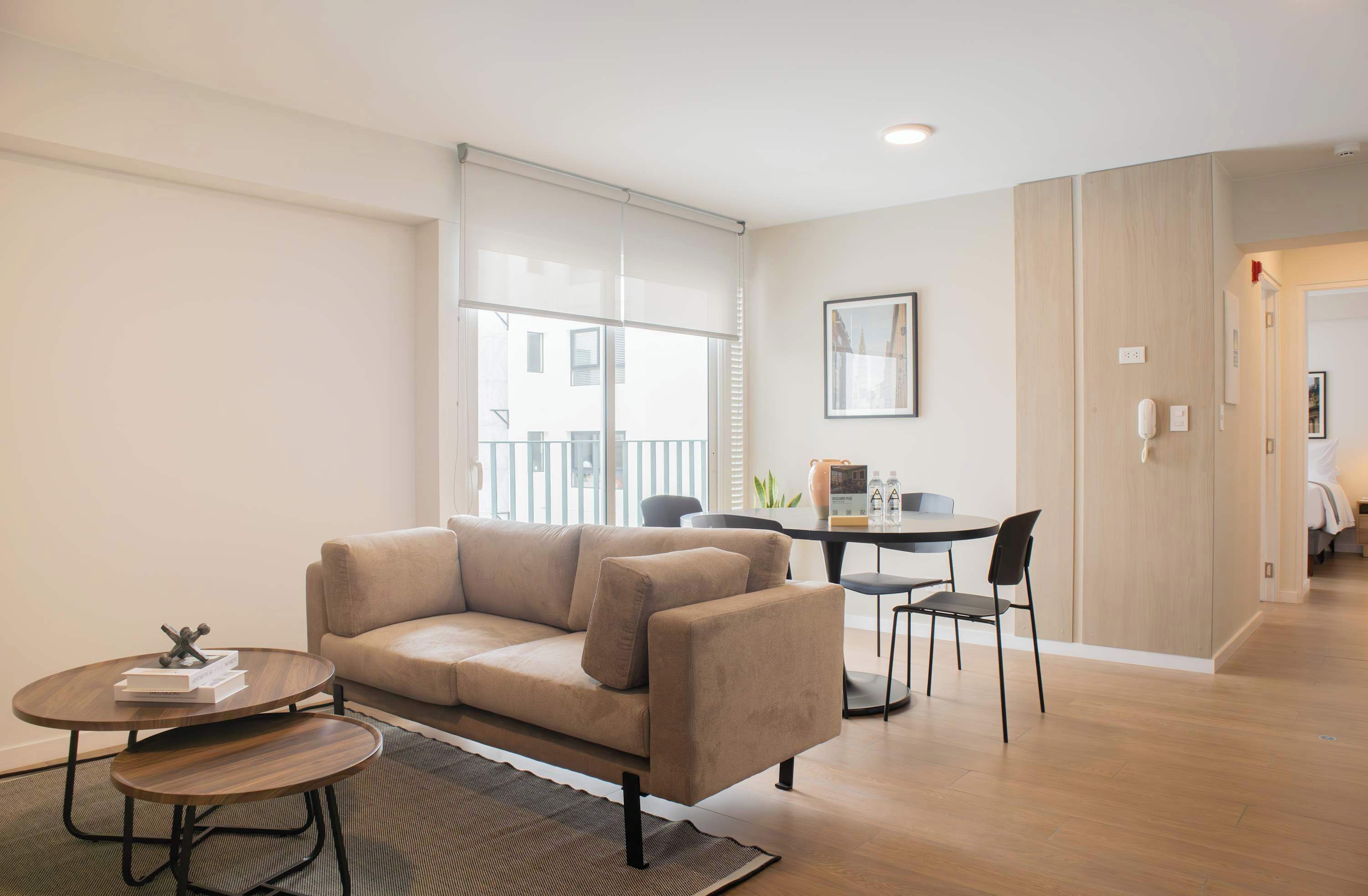 A modern living room with a beige sofa, a round coffee table, and a dining area with a small table and chairs.