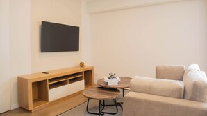 Una sala de estar moderna con un televisor de pantalla plana montado en la pared, una consola de madera, una mesa de centro redonda y un sofá color beige.