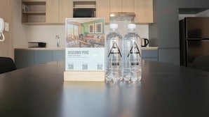 Una cocina moderna con armarios de madera, un microondas y un refrigerador. Hay dos botellas de agua sobre una mesa con un código QR y un letrero sobre una propiedad en Perú.
