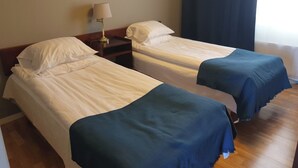 Quarto de hotel com duas camas de solteiro, uma mesa de cabeceira com abajur e uma janela com cortina.