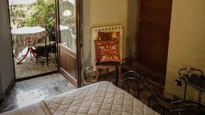 A bedroom with a bed, a chair, a small table, and a door leading to an outdoor area with a table and chairs.