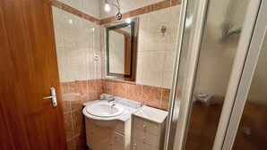 A bathroom with a wooden door, a sink with a mirror above it, and a shower area. - Apartman Velvet Vista 3 (Novi Vinodolski)