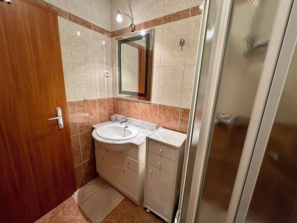 A bathroom with a wooden door, a sink with a mirror above it, and a shower area.