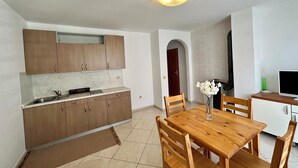 A compact kitchen with wooden cabinets, a built-in sink, and a dining area with a wooden table and chairs. - Apartman Velvet Vista 3 (Novi Vinodolski)