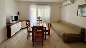 A compact living space with a dining area, a sofa, and a TV on a cabinet. - Apartman Velvet Vista 3 (Novi Vinodolski)