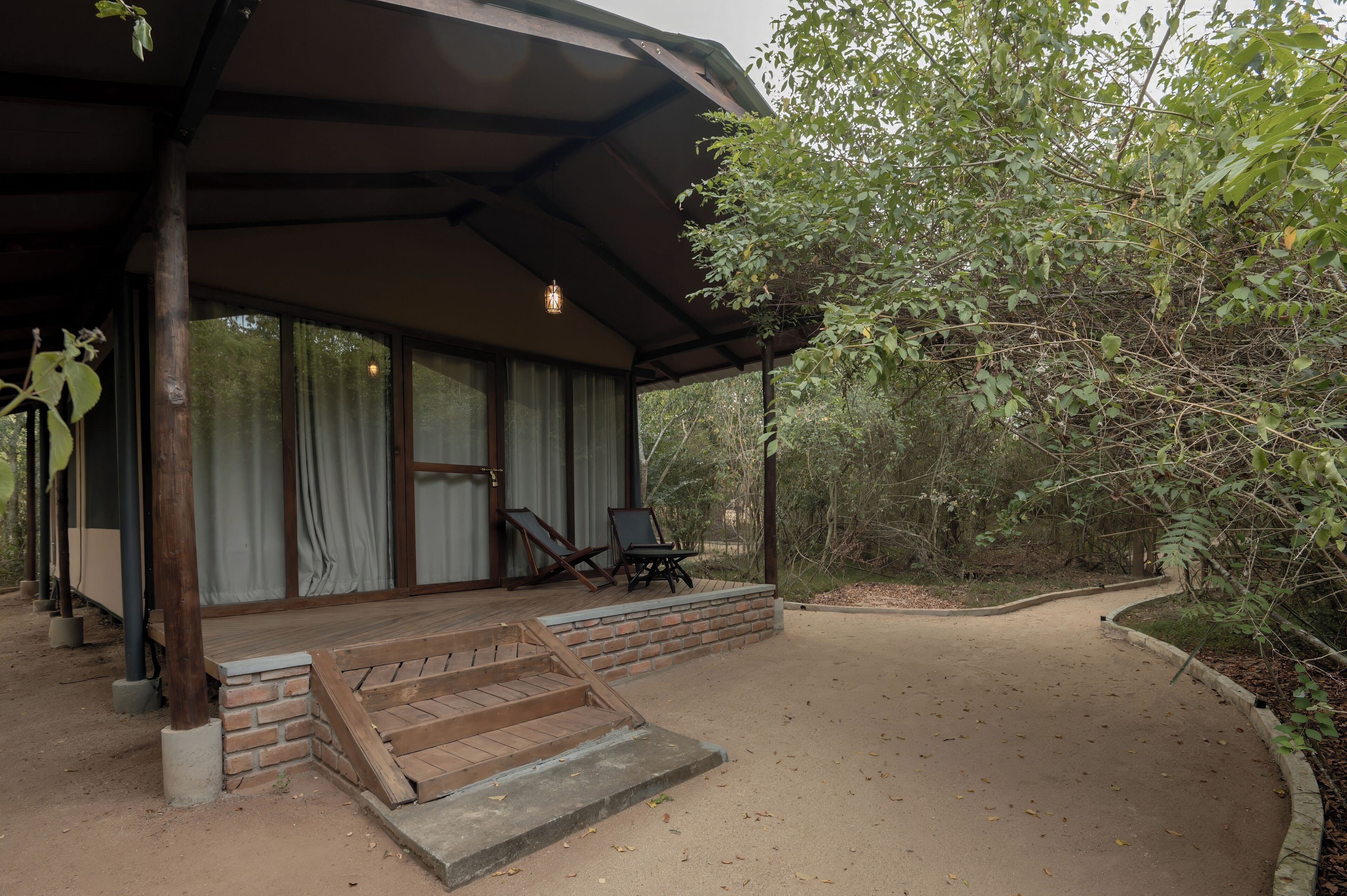A covered outdoor area with a wooden deck, two chairs, and a brick wall.