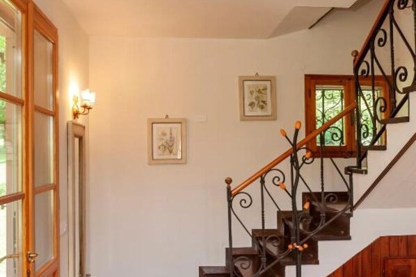 A staircase with ornate metal railings and wooden steps, leading to a landing with framed artwork.