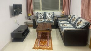 Uma sala de estar com um sofá, uma mesa de centro e uma TV fixada na parede.
