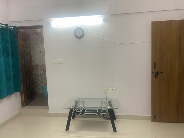 A room with a glass table, a wooden door, and a wall socket. - Srilakshmi Nivasa (Sahakaranagar, Bengaluru)