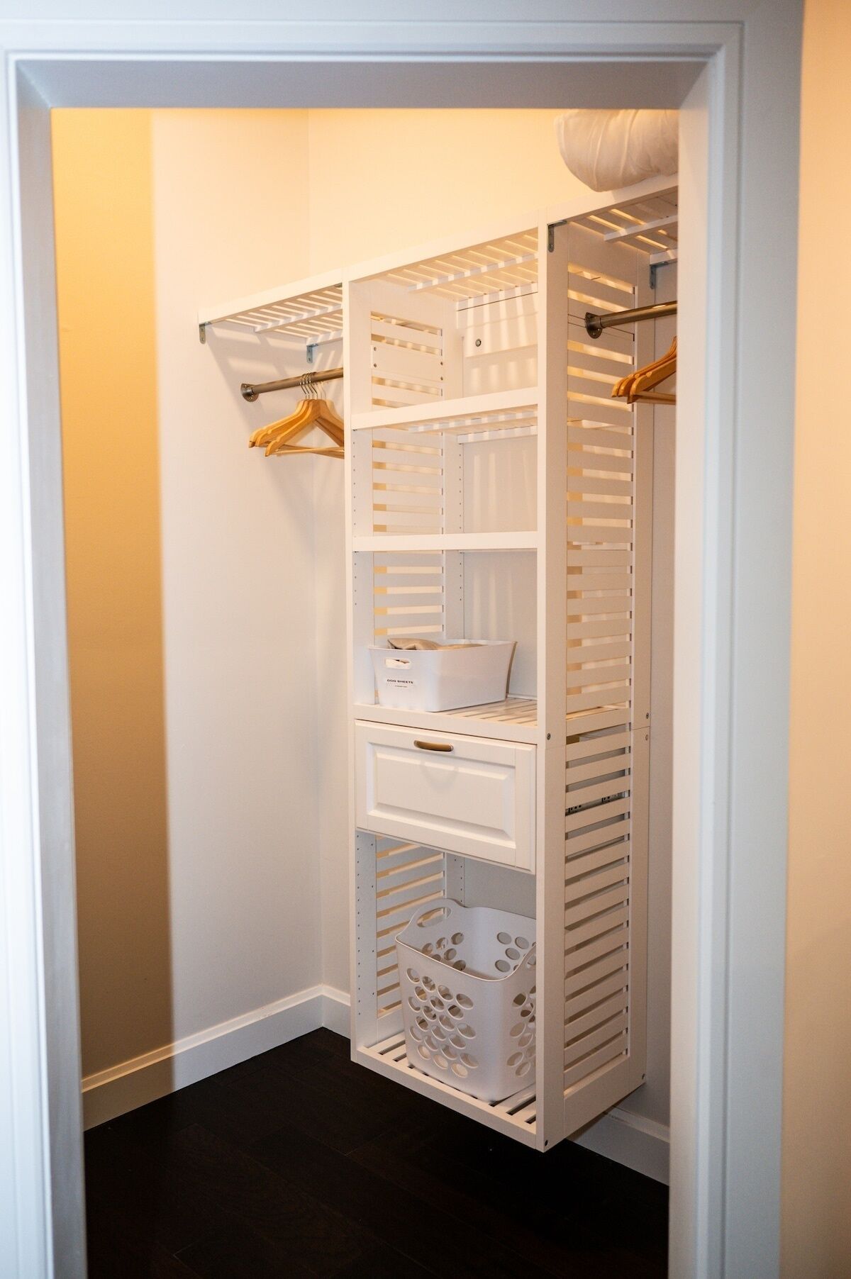 A white walk-in closet with multiple shelves, a hanging rod, and a storage bin.