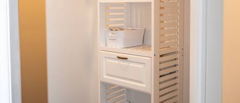 A white walk-in closet with multiple shelves, a hanging rod, and a storage bin.