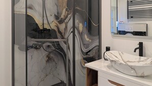 Une salle de bain moderne dotée d’une douche à parois de verre, d’un meuble-lavabo blanc avec un plan de toilette en marbre et d’un porte-serviettes mural.