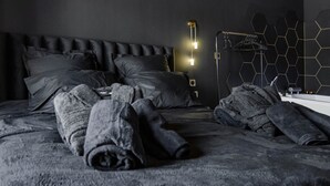 A bed with rolled-up blankets, a black headboard, and a wall-mounted light fixture.