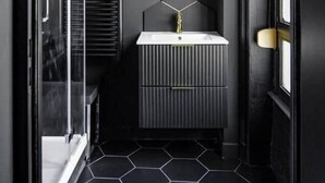 A modern bathroom with a black and white color scheme, featuring a round mirror, a white sink, and a black radiator.