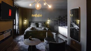A modern hotel room with a large bed, a TV, a unique ceiling light, and a mirror.