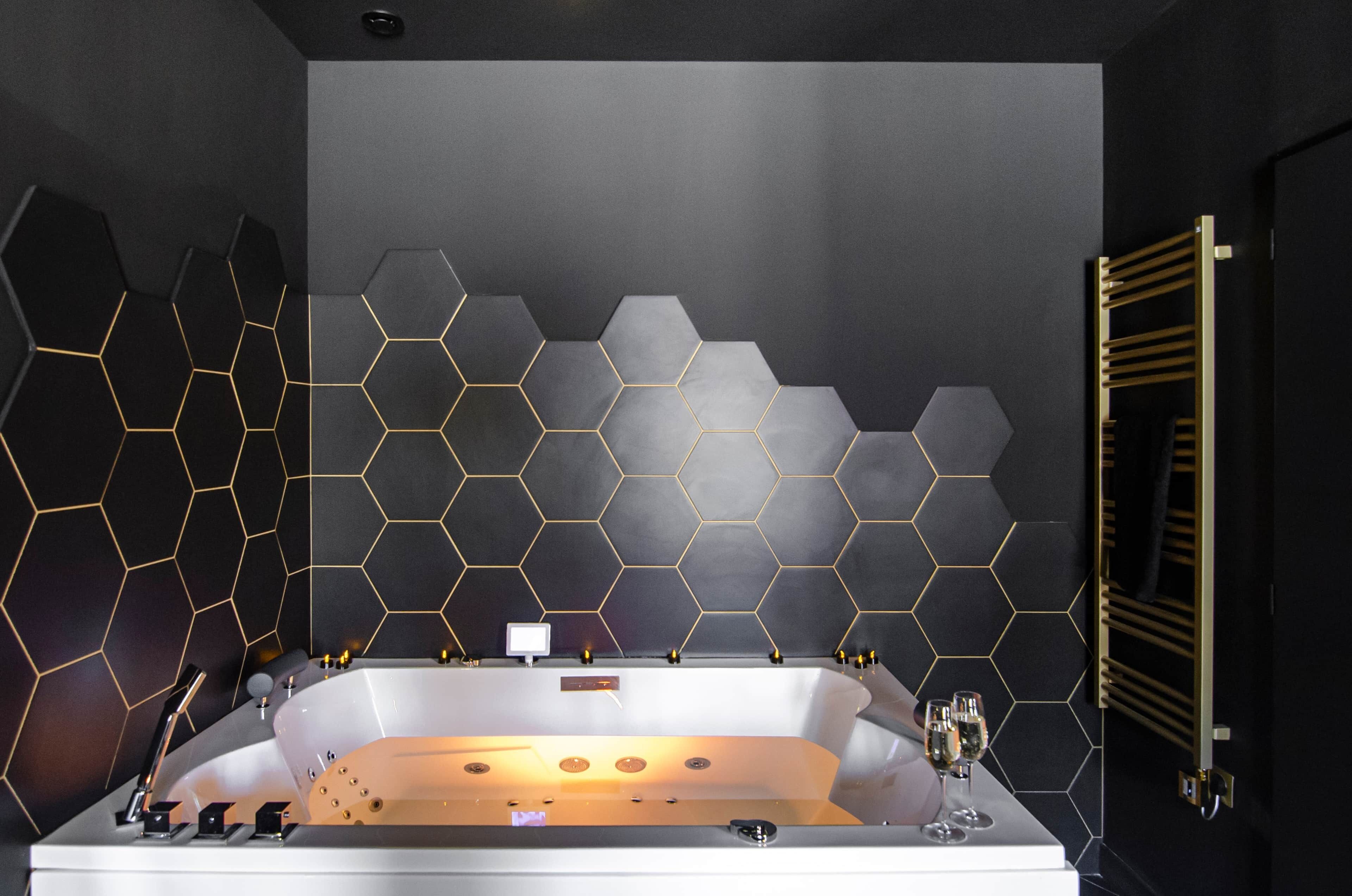 A modern bathroom with a large bathtub, a gold-tub surround, and a hexagonal wall design.