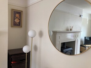 Une pièce avec une cheminée blanche, un miroir rond et un lampadaire.
