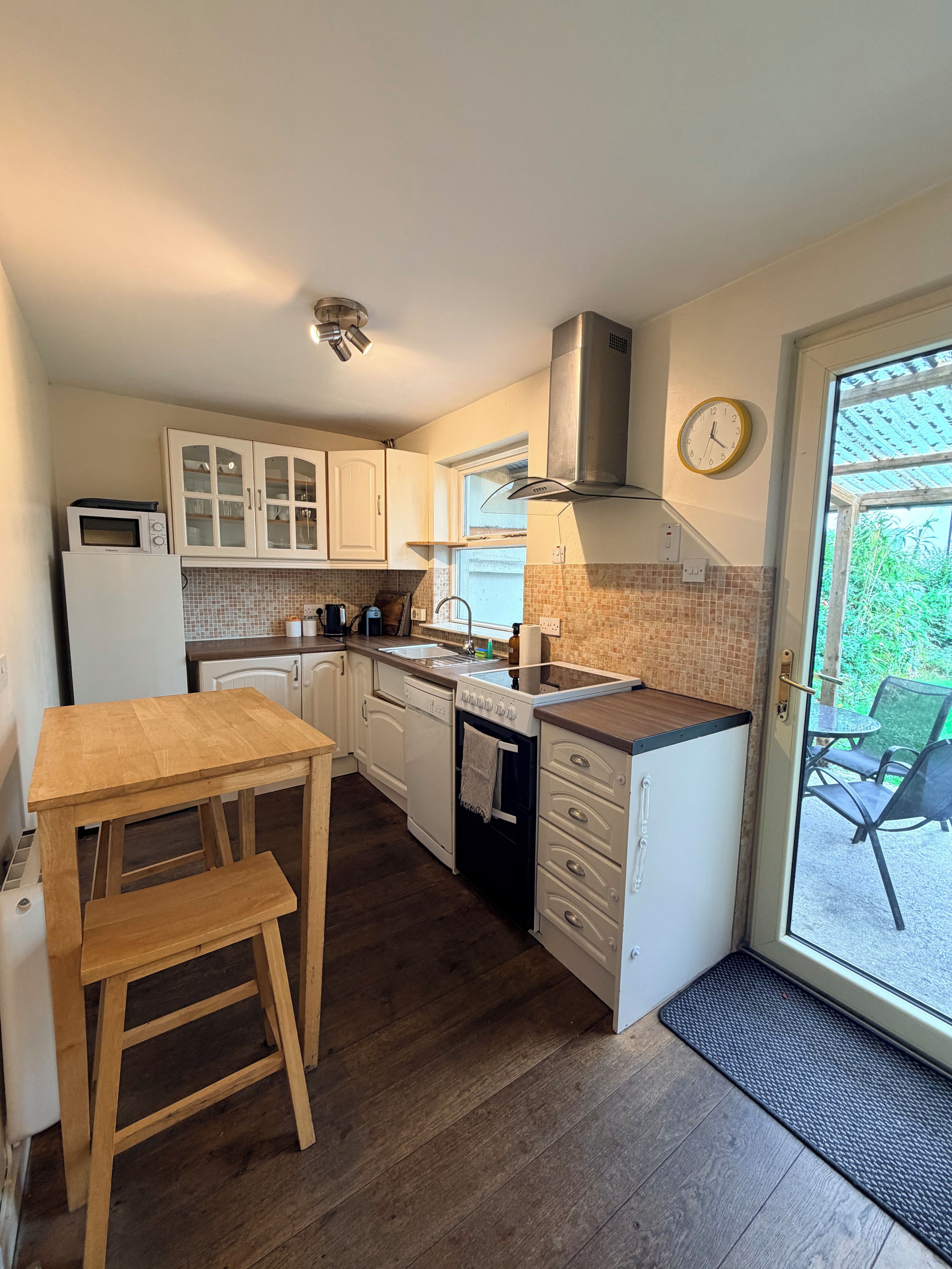 A compact kitchen with a wooden table and bench, a built-in oven, and a window overlooking greenery.