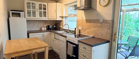 A compact kitchen with a wooden table and bench, a built-in oven, and a window overlooking greenery.