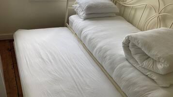A single bed with white bedding and pillows, a window with a view of greenery, and a wooden floor.
