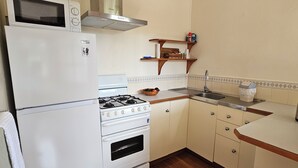 A compact kitchen with a refrigerator, stove, microwave, and sink. - Fletcher Christian Apartments - Isabella Suites (Burnt Pine)