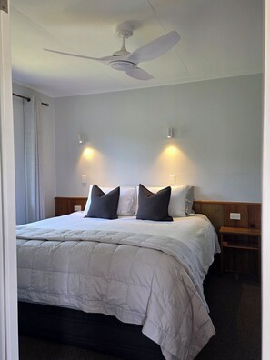Een hotelkamer met een bed, een plafondventilator, twee wandlampen en een houten nachtkastje.