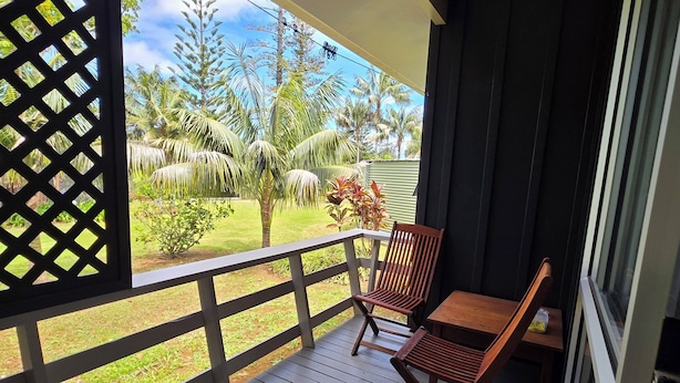 A wooden deck with two rocking chairs and a table, overlooking a garden with palm trees and a clear sky. - Fletcher Christian Apartments - Isabella Suites (Burnt Pine)