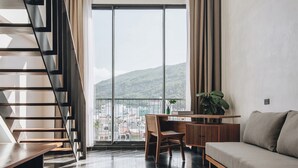Un salon moderne avec un escalier, un canapé, une table à manger et une vue sur le paysage urbain, visible à travers de grandes fenêtres.