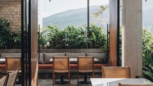 Un espace extérieur moderne, aménagé avec des meubles en osier, un mur en pierre et offrant une vue sur la verdure et les montagnes.