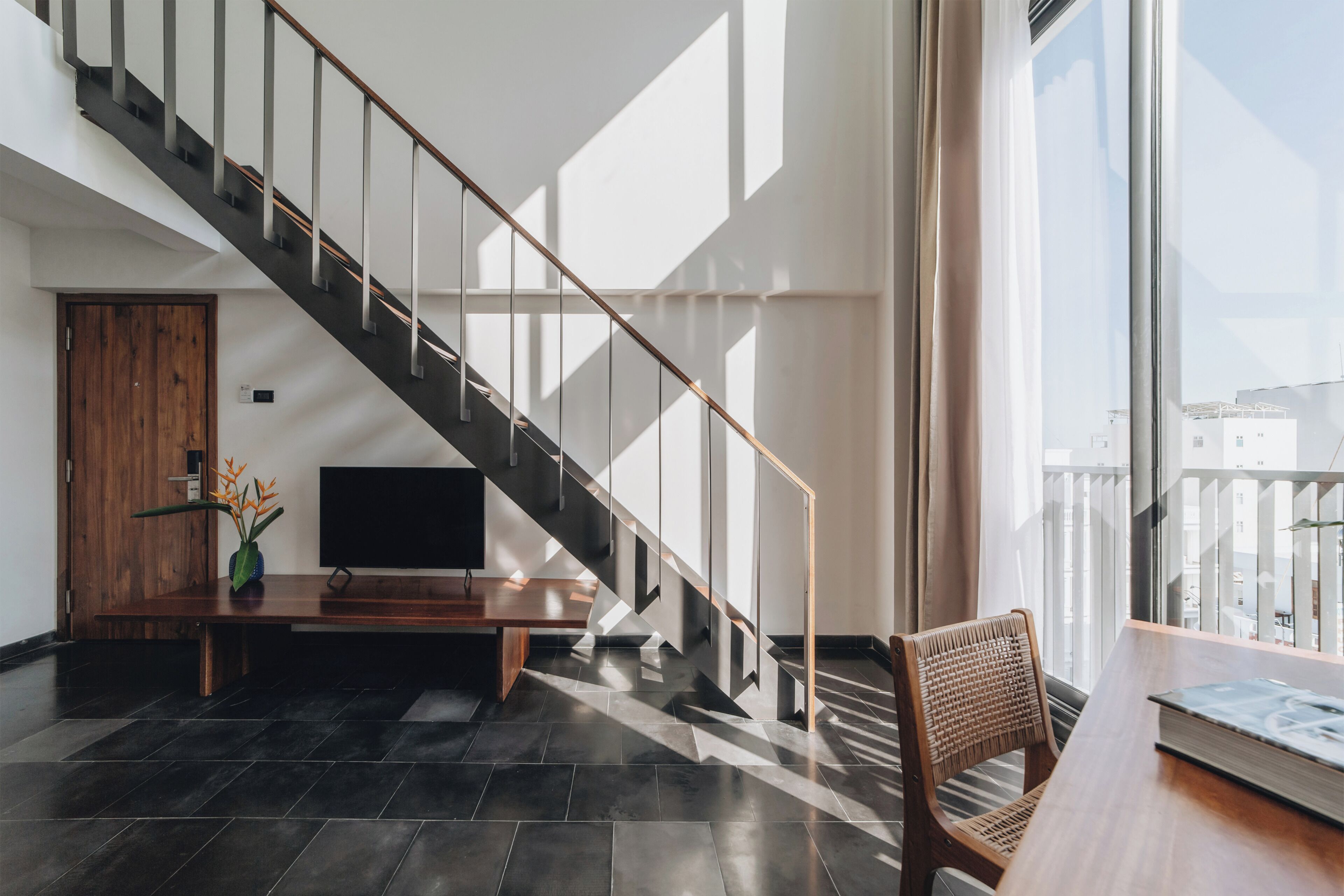 A modern interior with a staircase, a flat-screen TV, a wooden door, and a wicker chair.