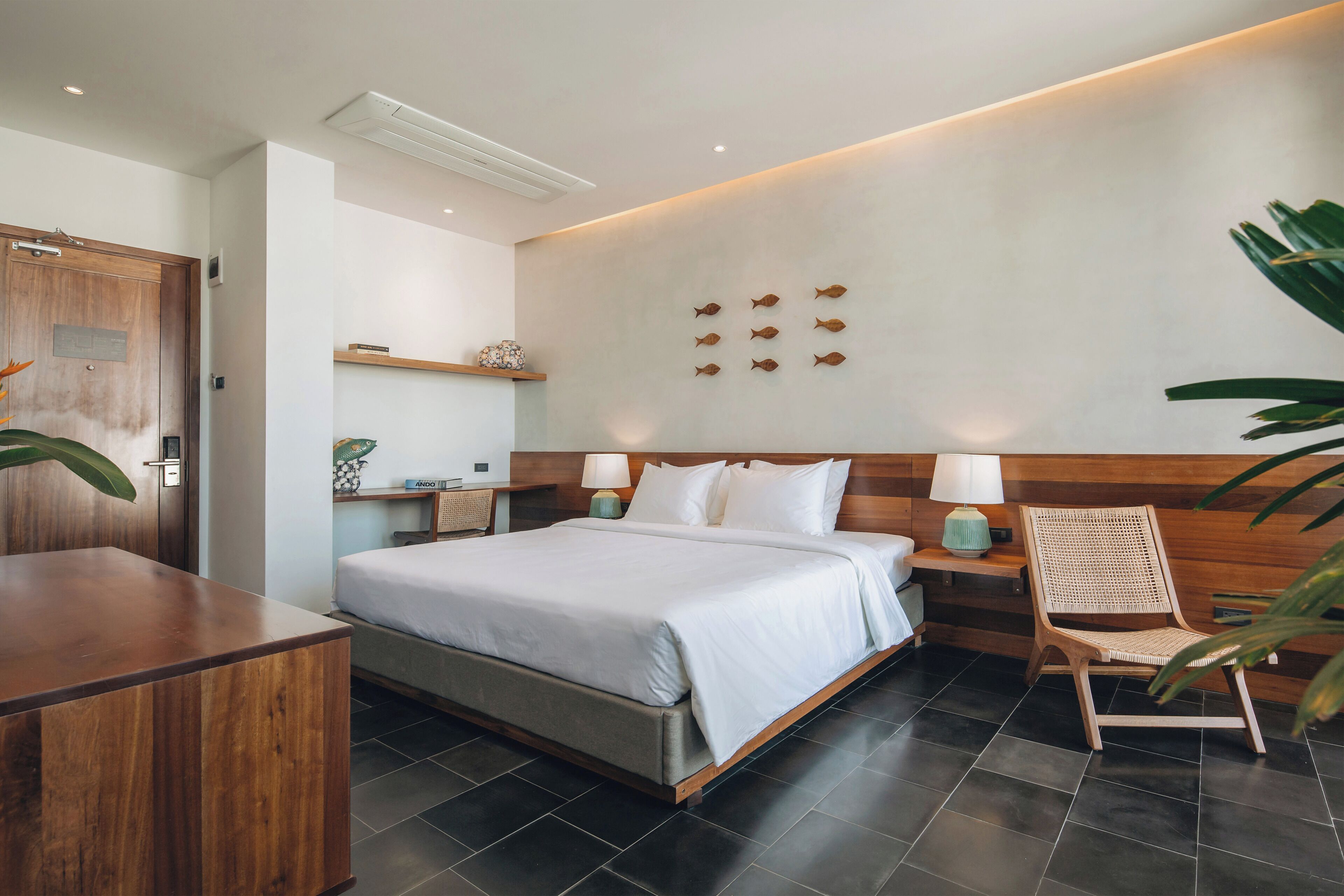 A modern hotel room with a large bed, bedside tables, a wooden headboard, and a wall-mounted shelf.